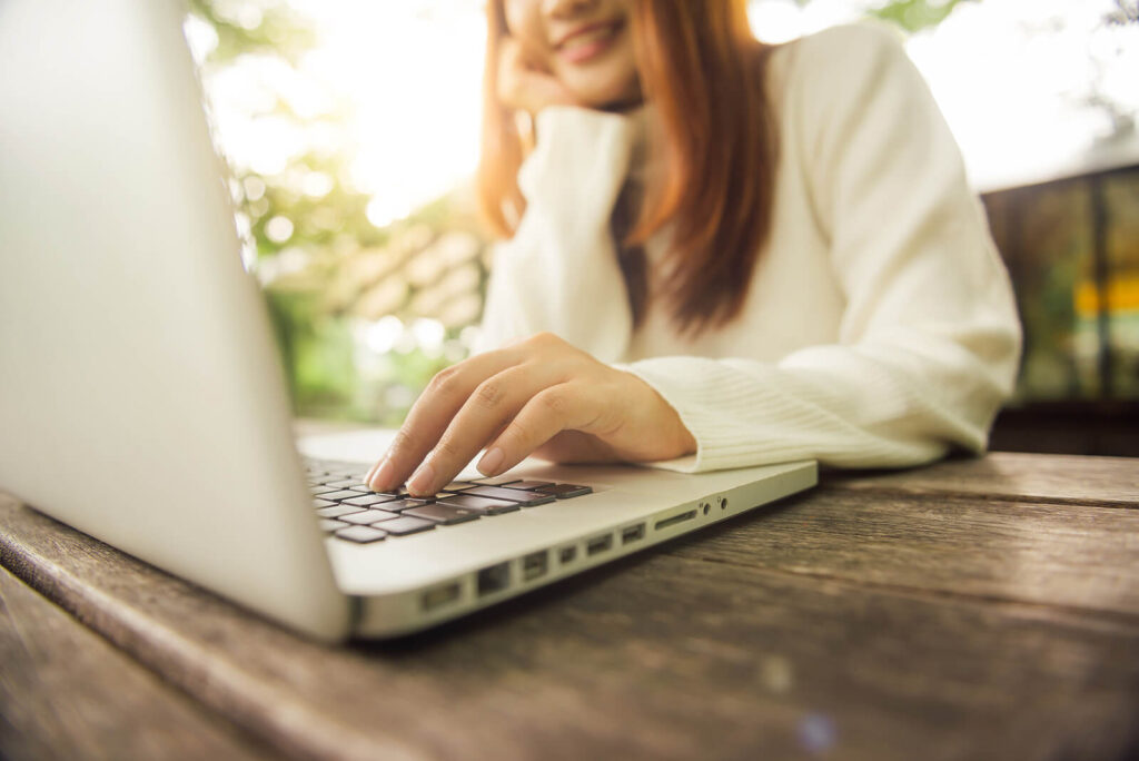 Image of a smiling woman sitting at a desk typing on a laptop. Overcome the grip of your eating disorder and cope in healthy ways with the help of eating disorder recovery coaching in the UK.