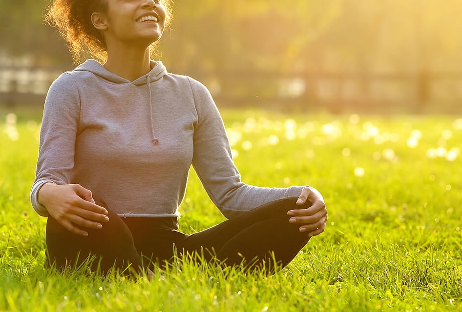 Image of a smiling woman sitting on the ground looking up toward the sky. Begin your healing journey and start recovering from your eating disorder with the help of eating disorder recovery coaching in the UK.