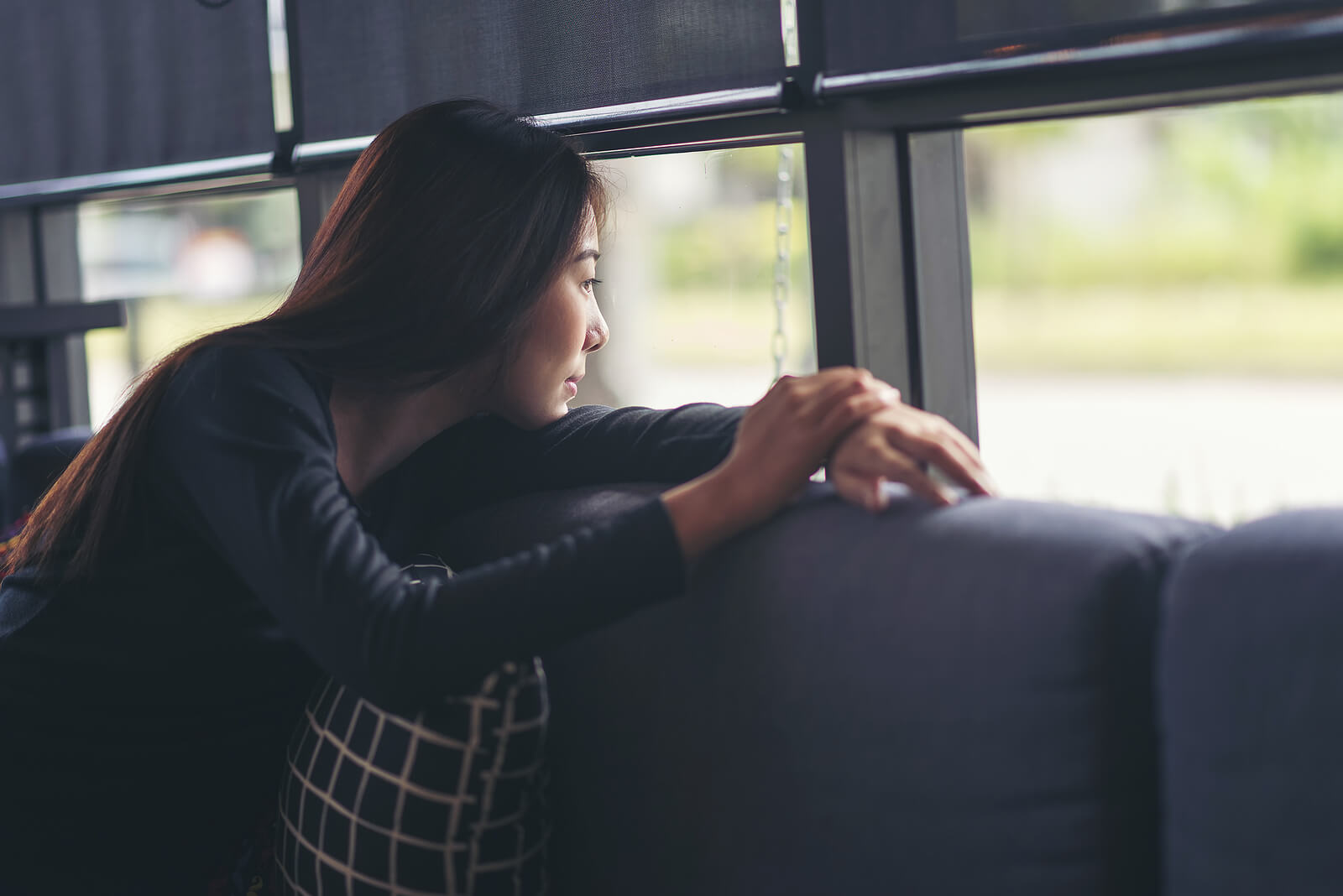 Image of a thoughtful woman sitting on a couch looking out a window. Find a safe space exploring your eating disorder and begin healing with eating disorder recovery coaching in the United Kingdom.