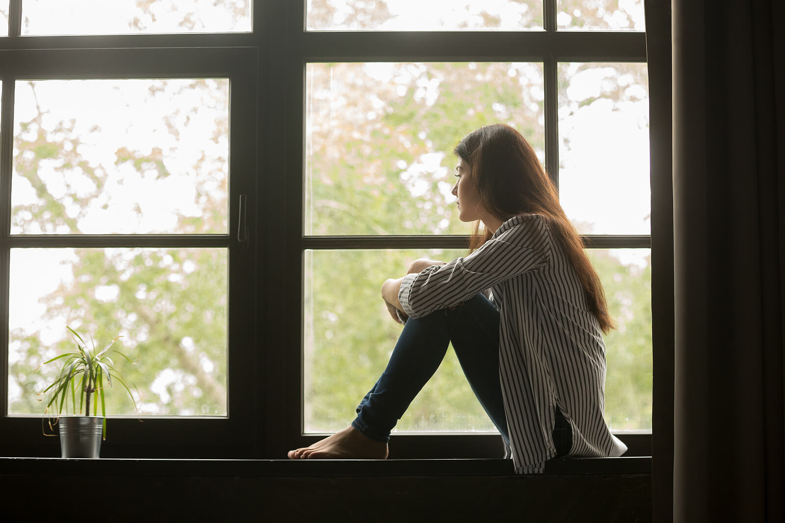 Image of a thoughtful woman sitting by a window looking out. With the support of a skilled eating disorder recovery coach in the UK you can begin healing your body and relationship with food. Reach out to Healthy Self Recovery to get started!