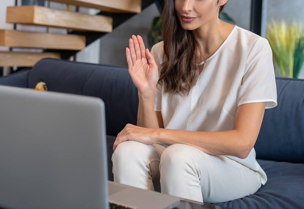 Image of a woman sitting on a couch waving at a laptop. This image represents how you can begin creating a healthier relationship with your body with the support of eating disorder recovery in the UK.