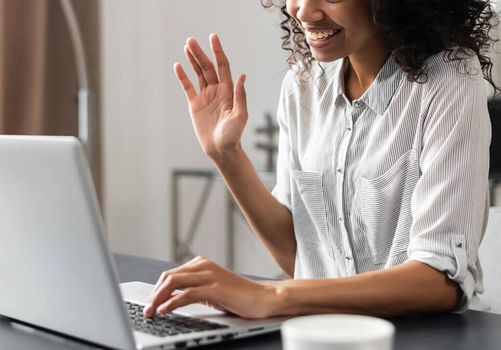 Image of a smiling woman sitting at a desk waving at a laptop. Begin making positive changes when it comes to your eating disorder, and start healing with eating disorder recovery coaching in the United Kingdom.