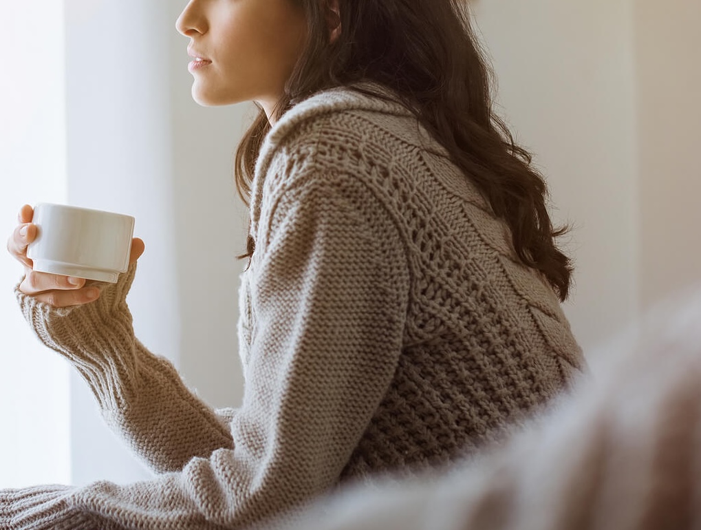 Image of a peaceful woman holding a coffee mug while sitting up in bed looking out a window. Recovery can be overwhelming, but with the support of eating disorder recovery coaching in the UK you can begin breaking free from your eating disorder's grip.