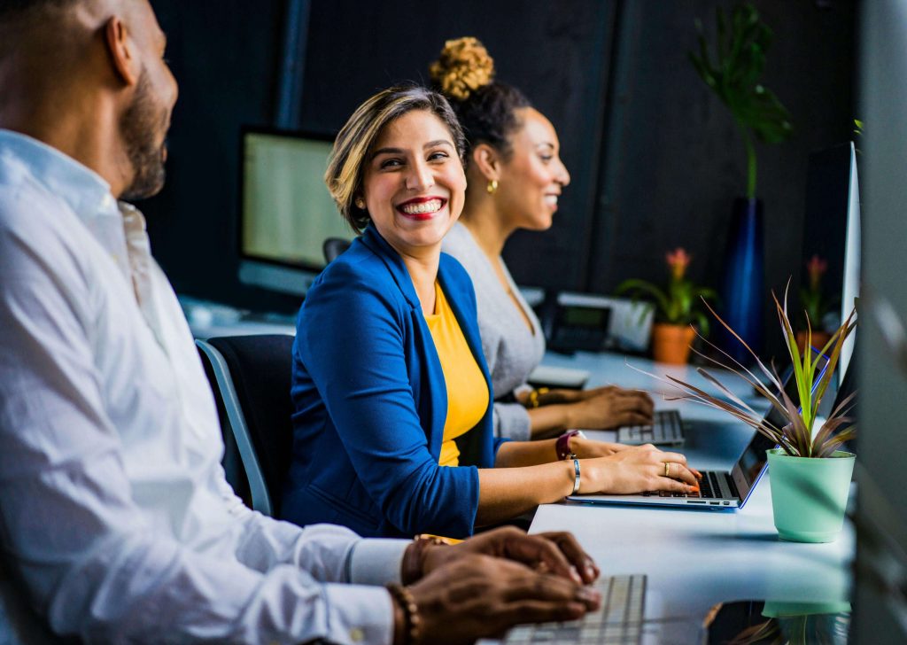 happy professionals | eating disorder recovery coaching in the uk | eating disorder recovery coach in the uk | eating disorder coaching | british eating disorder recovery coach | England | Scotland | Ireland Image of a smiling professional woman sitting between two other happy professionals at a desk. Struggling with an eating disorder as a busy professional can be hard to overcome alone. With eating disorder recovery coach in the UK you can start to heal soon.
