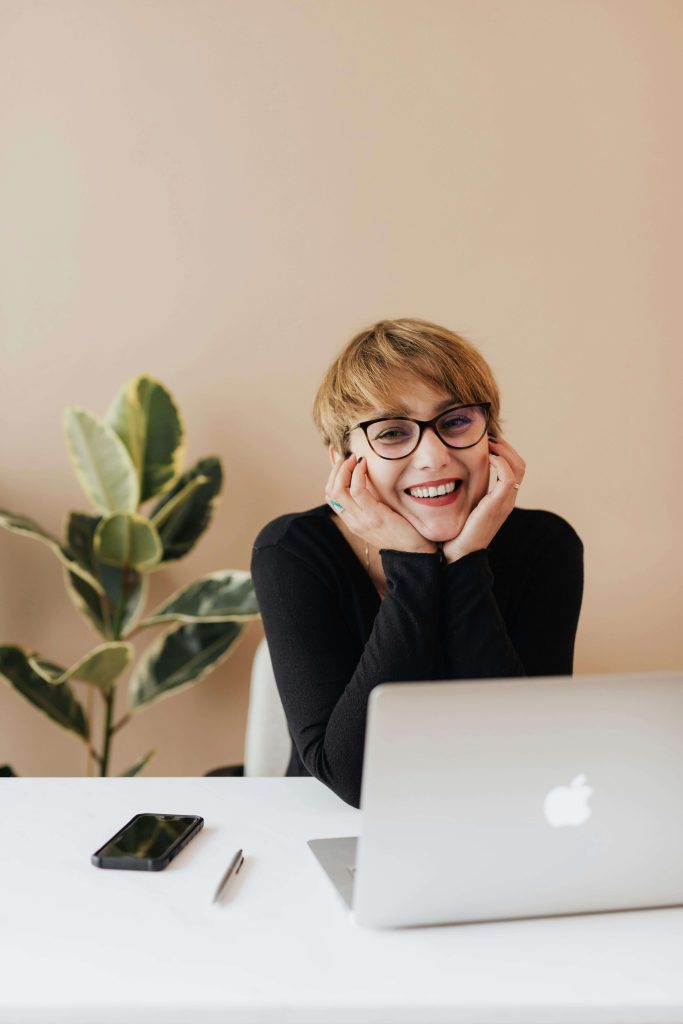 Smiling woman sitting at a desk with a laptop. Learnt o develop coping strategies and manage your anxiety around food with the help of a skilled eating disorder recovery coach in the UK.