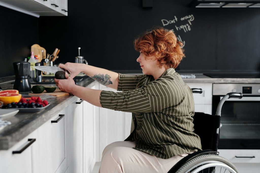 Woman in a wheelchair in a kitchen cutting an avocado. Learn to overcome the fear of certain foods with meal support used in eating disorder recovery coaching in the UK.