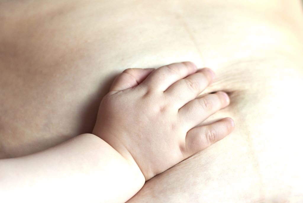 Baby's hand on mom's stomach. Postpartum can be overwhelming, especially when struggling with an eating disorder. Find support when it comes to rebuilding trust with your body with eating disorder recovery coaching in England. 