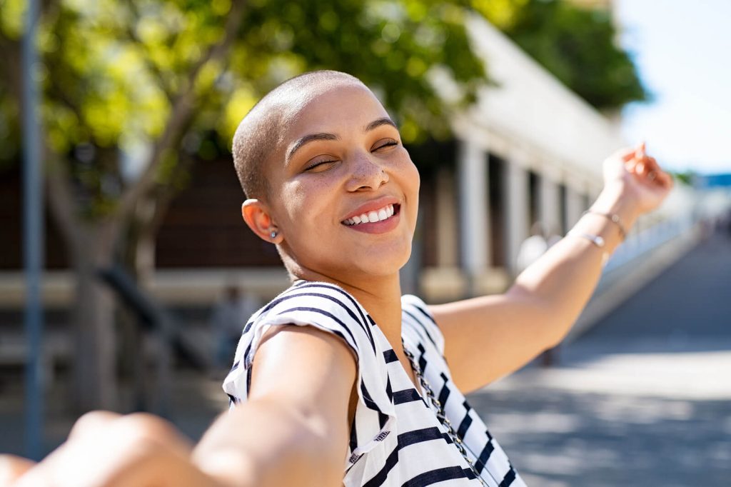 Smiling woman standing outside on a sunny day with her eyes closed. Start your path to recovery and begin healing from your eating disorder with the help and support of a skilled British eating disorder recovery coach in the UK.