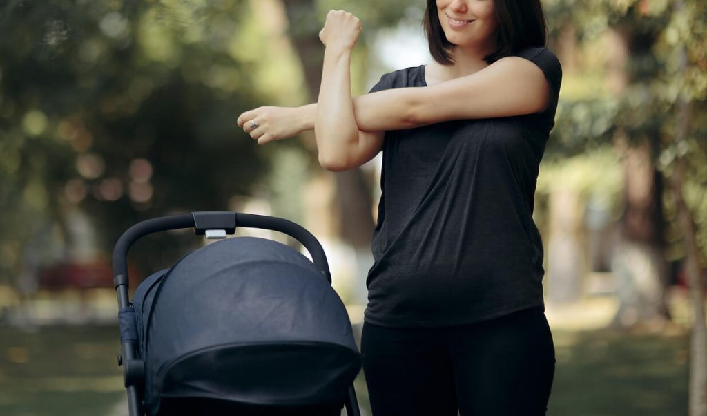 Smiling woman standing in a park stretching next to a baby stroller. Find support when it comes to recovery from a postpartum eating disorder with the help of a British eating disorder coach in the UK.