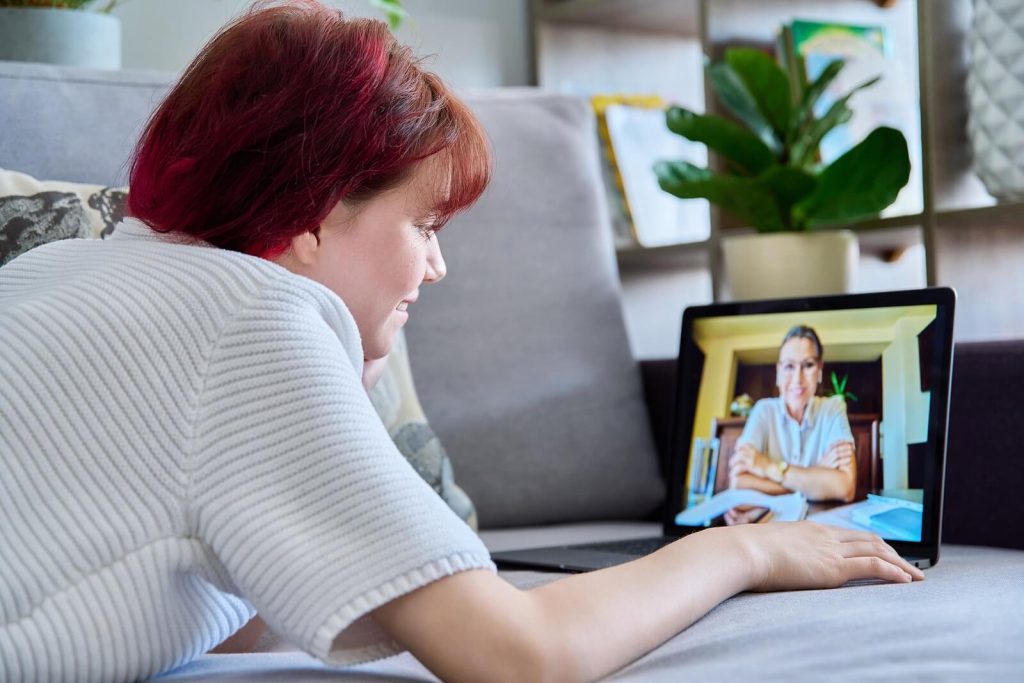 Young woman with red hair laying on a couch using a laptop to access online therapy. With eating disorder recovery coaching in the UK you can begin to change your thought patterns and beliefs that surround your eating disorder and begin healing.