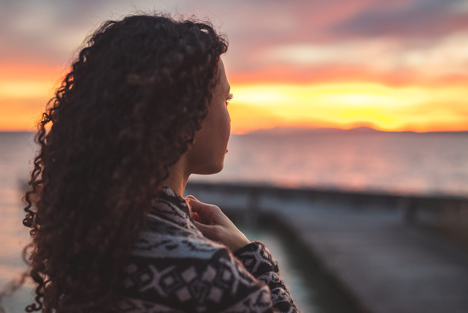 Peaceful woman looking out at the ocean as the sun sets. Find ongoing support during your recovery with the help of a compassionate eating disorder recovery coach in the UK.