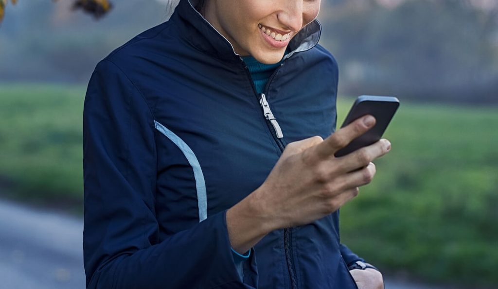 Smiling woman outside holding a cell phone and texting. Stay on track with your weekly recovery goals with messaging support in eating disorder recovery coaching in the UK.