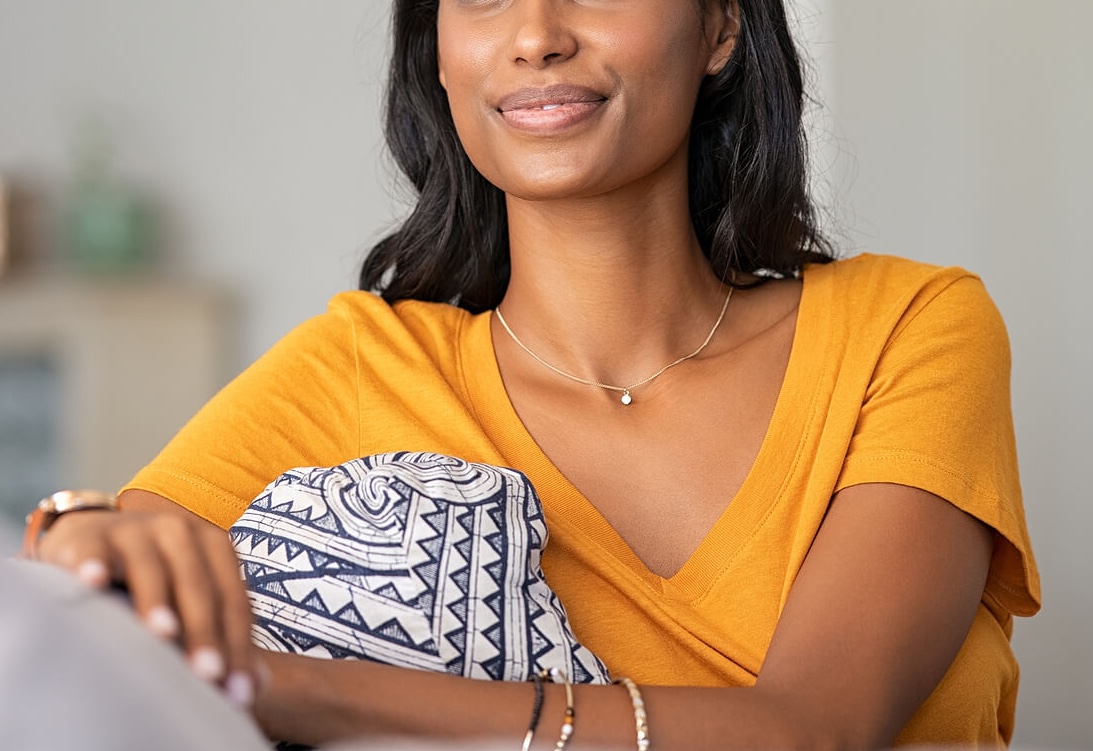 Relaxed smiling Indian woman sitting on a couch. With the support of holistic eating disorder recovery coaching in the UK you can begin to improve your physical and mental well-being in positive ways.
