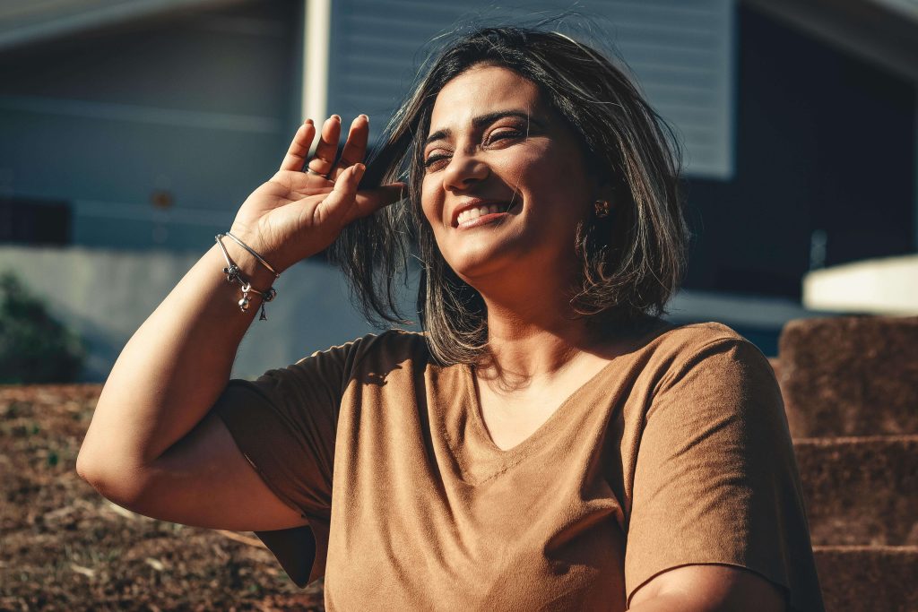Smiling woman standing outside brushing her hair out of her face. Begin to regain control of your eating disorder and move toward lasting recovery with eating disorder recovery coaching in the UK.