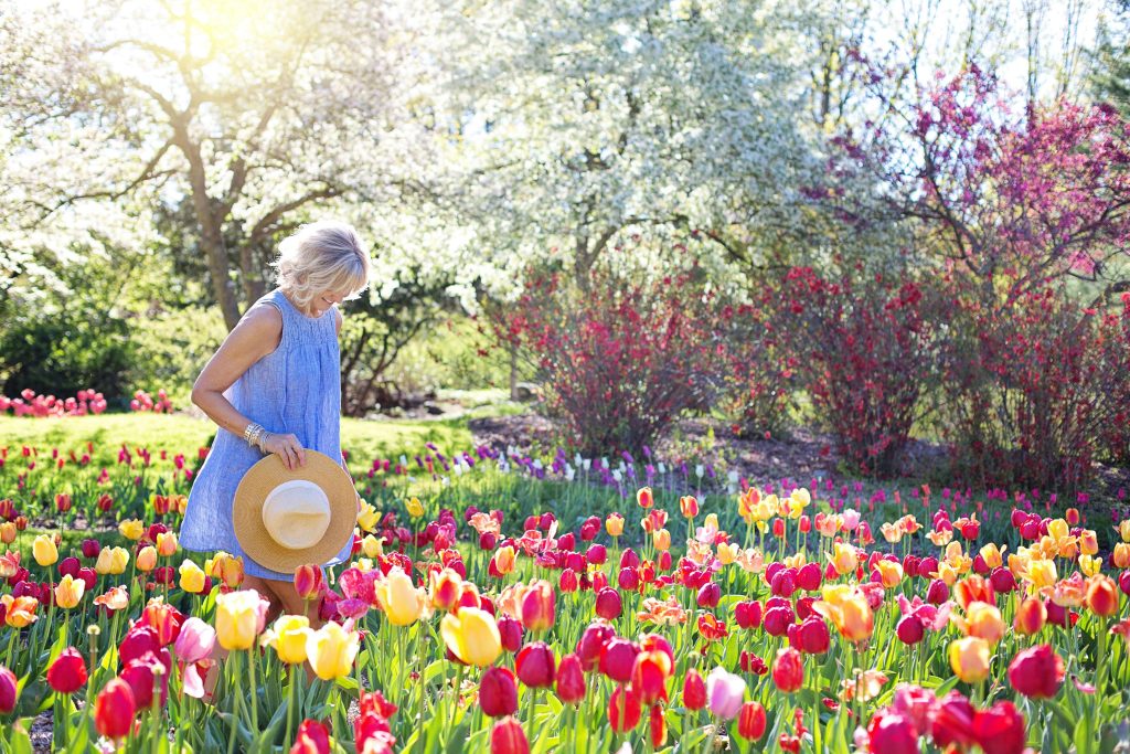 Happy woman standing in a patch of colorful tulips on a sunny day. With the help of eating disorder recovery coaching in the UK you can begin to find compassionate support to help you as you recover.