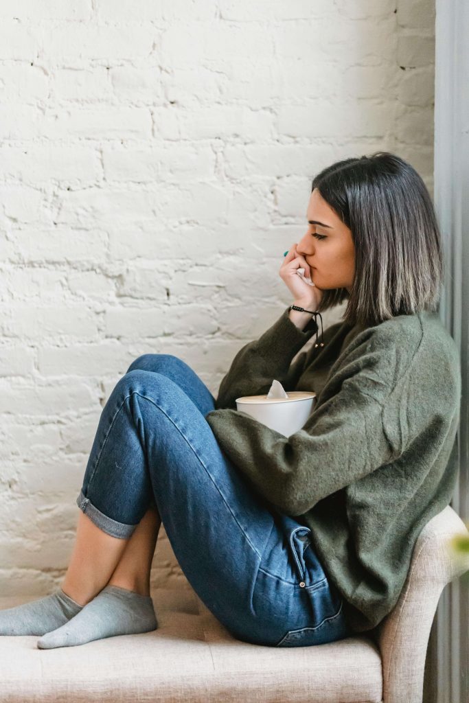 Anxious woman sitting on a chair resting her hand against her mouth. Find support in coping from your eating disorder symptoms with the help of eating disorder recovery coaching in the UK.