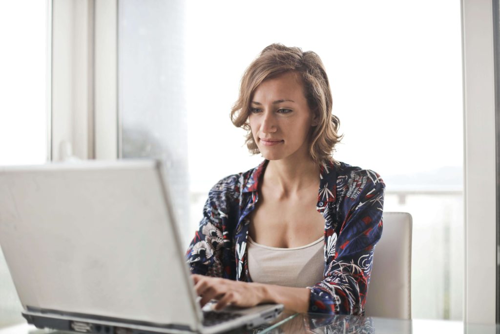 Smiling woman sitting at a table working on a laptop. Learn to reframe your disordered thoughts and begin healing from your eating disorder with eating disorder recovery online in the UK.