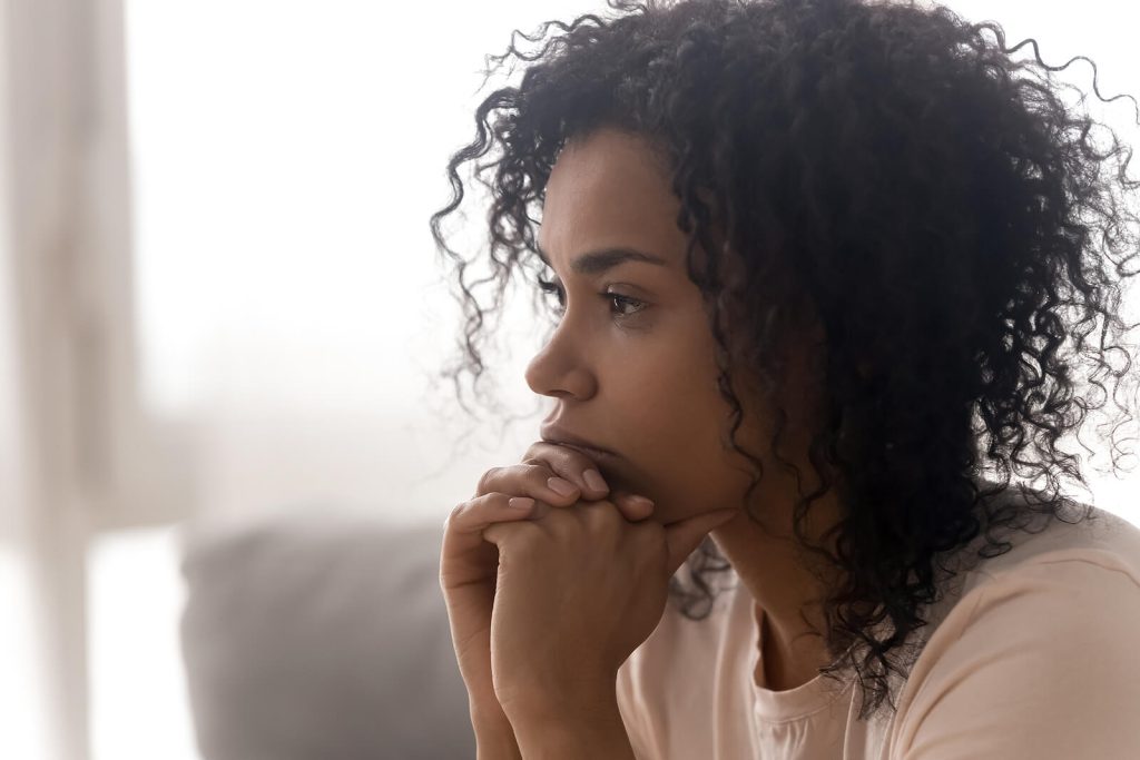 Thoughtful woman sitting on a couch looking off into the distance. Find support that can help you better understand and heal from your eating disorder with the help of an eating disorder recovery coach in the UK.
