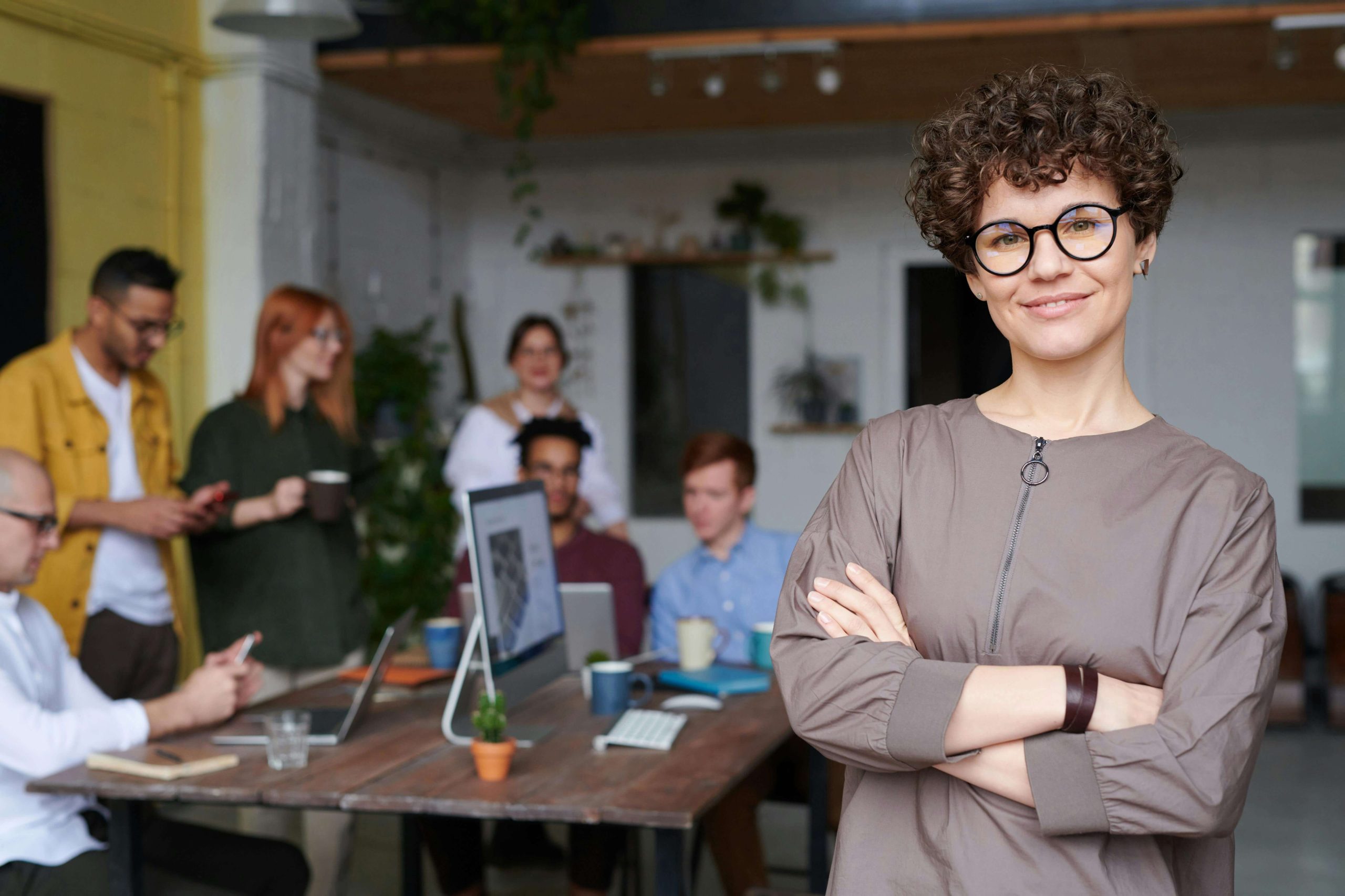 Happy professional woman standing in front of a group of professionals working. Break free from clean eating as a professional and heal your relationship with food with eating disorder recovery coaching in England.