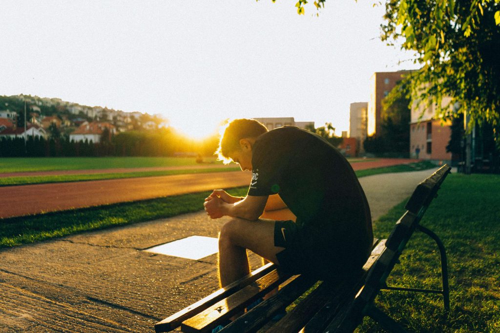 Sad athletic man sitting on a bench resting. Being an athlete can cause stress with food and exercise. With the support of a British eating disorder recovery coach you can begin to heal.