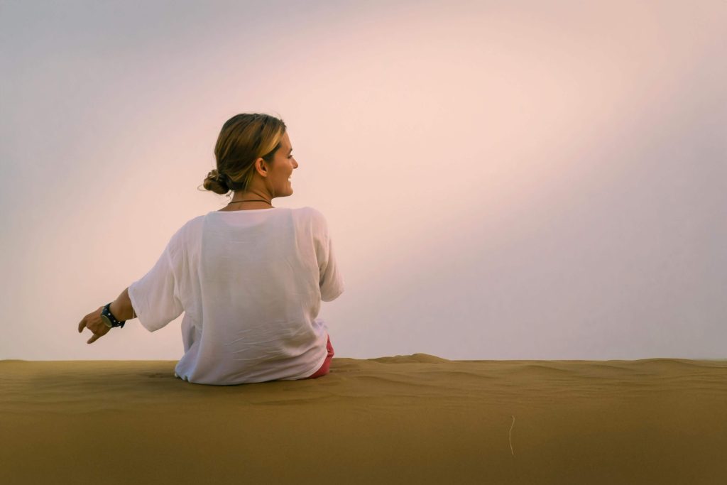 Happy woman sitting in the sand. With eating disorder recovery coaching in England, you can begin healing from your eating disorder and stay on track with day to day support. 