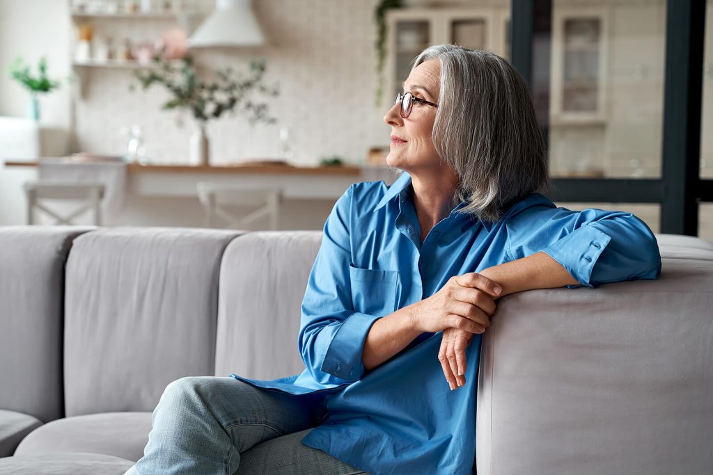 Mature woman sitting on a couch smiling. With eating disorder recovery coaching in England you can begin taking back control of your life where food no longer controls you. Start healing soon.