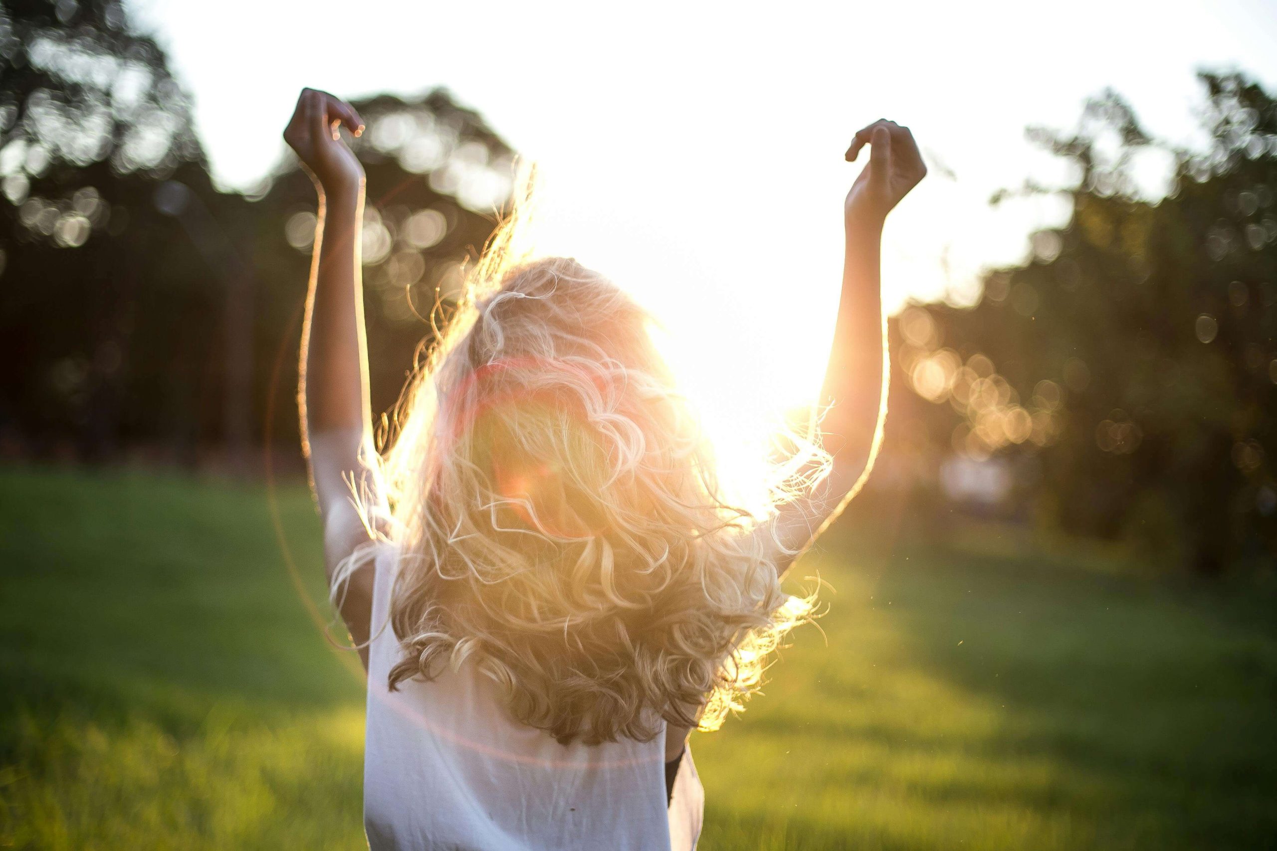 Happy woman standing outside as the sun sets with her arms raised. Find peace from your eating disorder and begin to recovery in healthy ways with eating disorder recovery coaching in England.