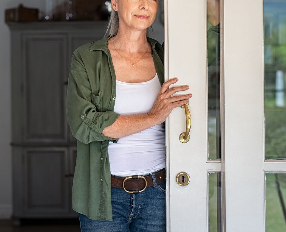 Thoughtful older woman in a green shirt standing in a doorway, looking reflective. A British eating disorder coach can help you reflect on your triggers and build confidence in recovery, no matter your stage of life.
