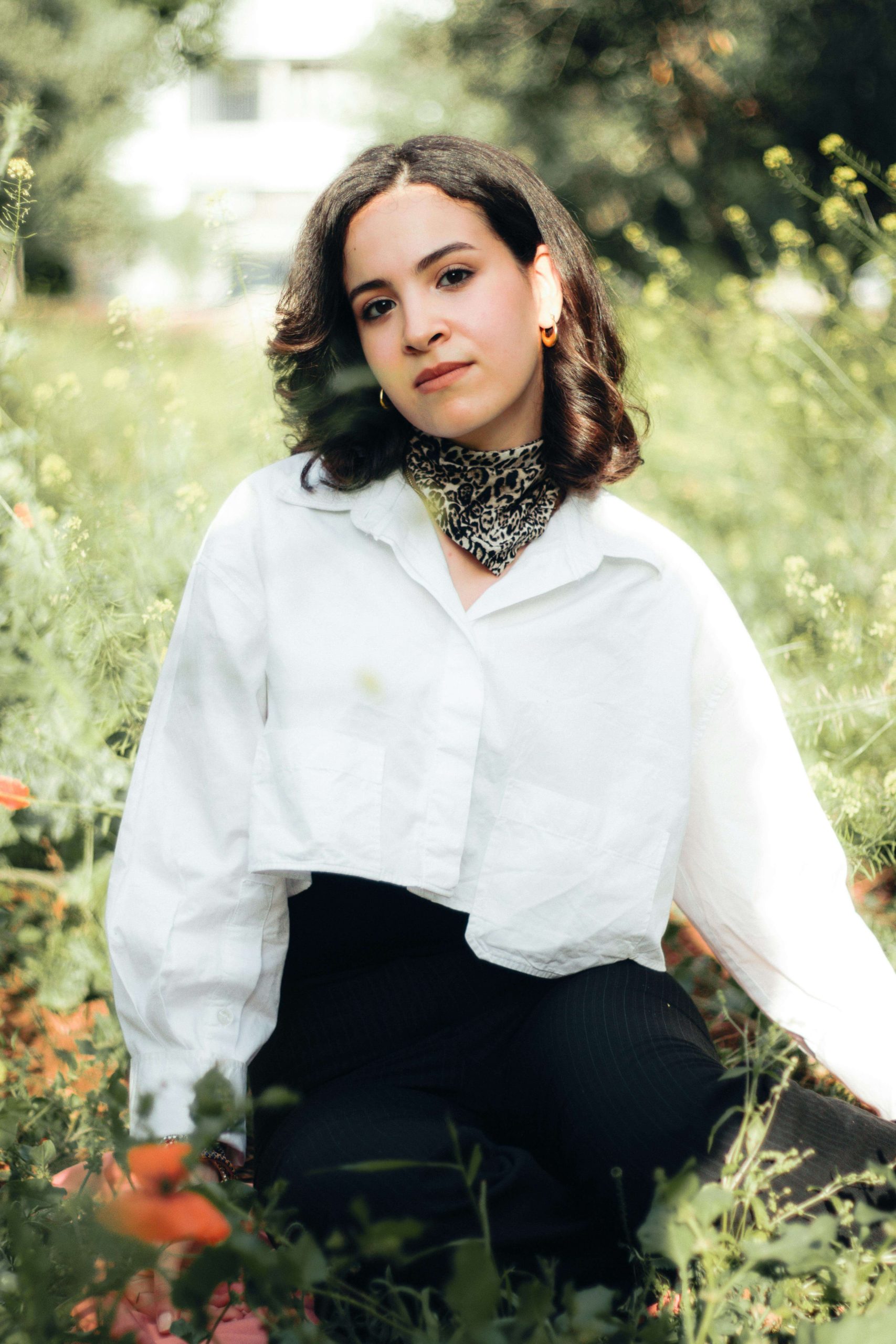 Young woman sitting in a field of flowers, calm and reflective. Find support from an ED recovery coach to redefine your sense of self with eating disorder recovery coaching in the UK.