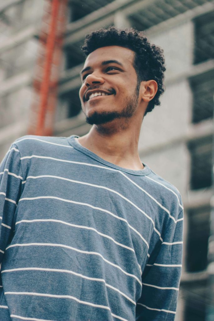 Young man smiling while standing outside in front of a building. Find encouragement and guidance with an ED recovery coach in England to rebuild confidence and balance after an eating disorder.