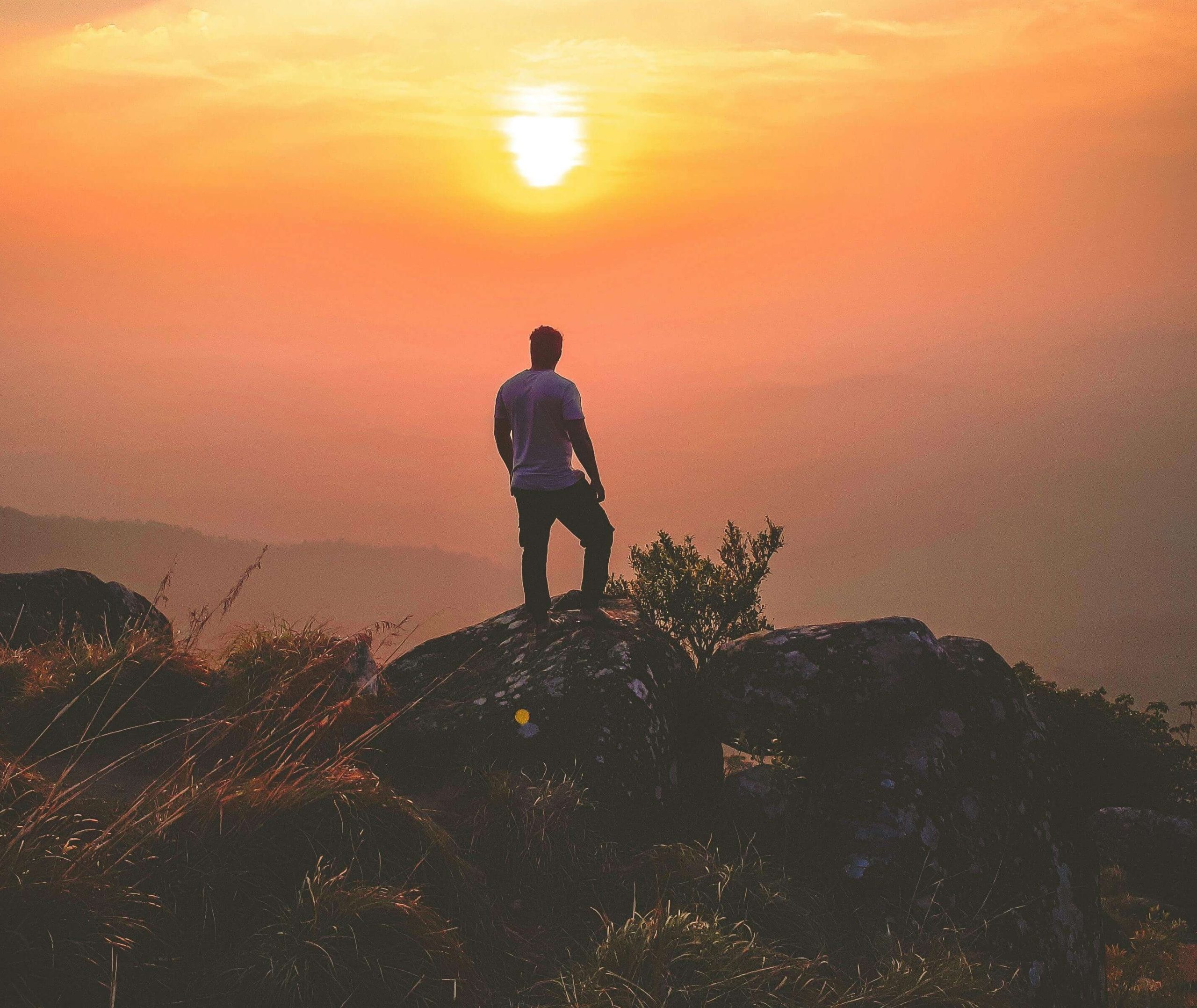 A man stands tall on a rock, looking toward the glowing sunset sky, symbolizing hope and strength. Begin your anorexia recovery journey and embrace healing with the support of eating disorder recovery coaching in England, guided by a British eating disorder recovery coach.