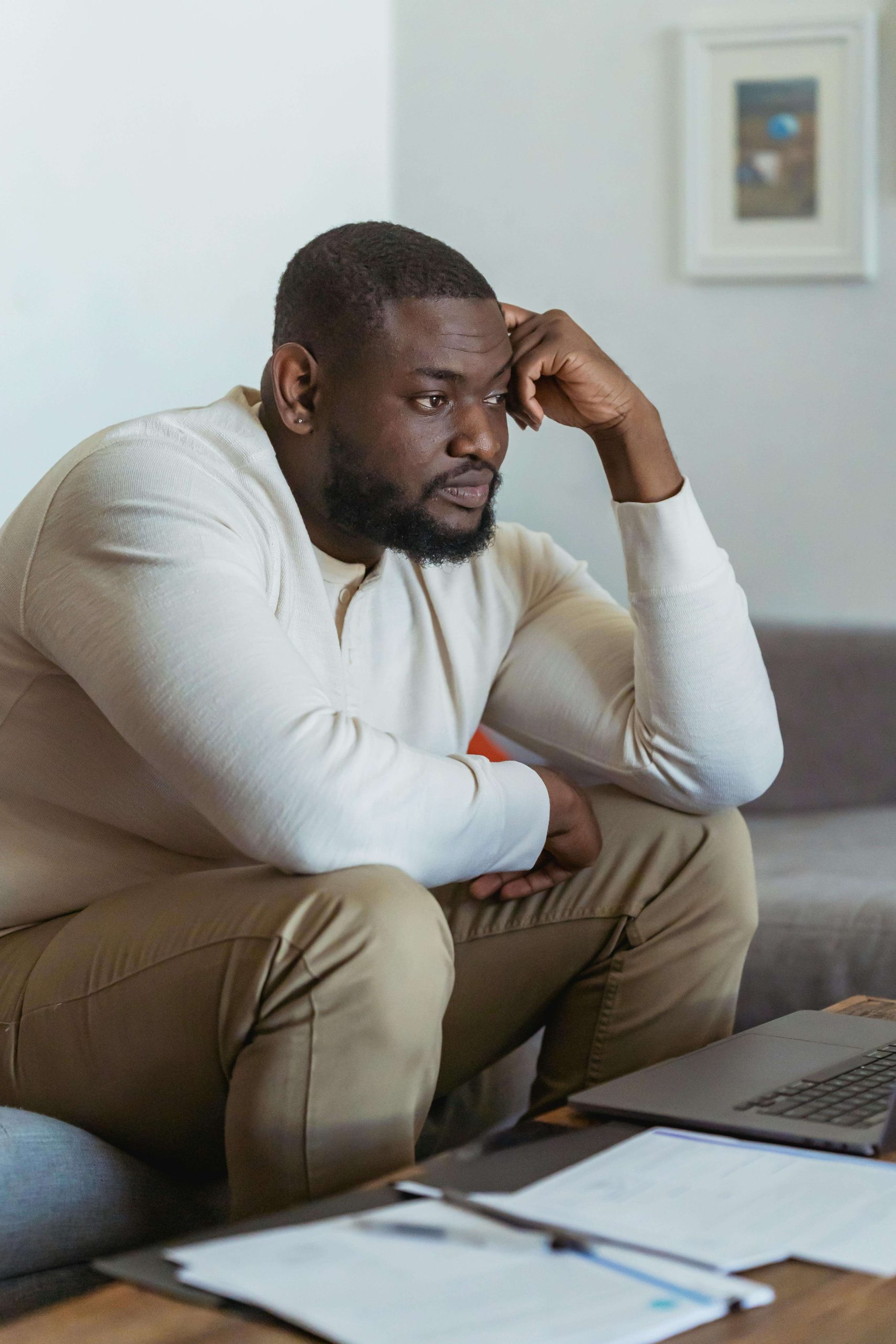 Stressed man sitting on a couch resting a hand against his head. If you struggle with anorexia, find support when it comes to healing with eating disorder recovery coaching in England.