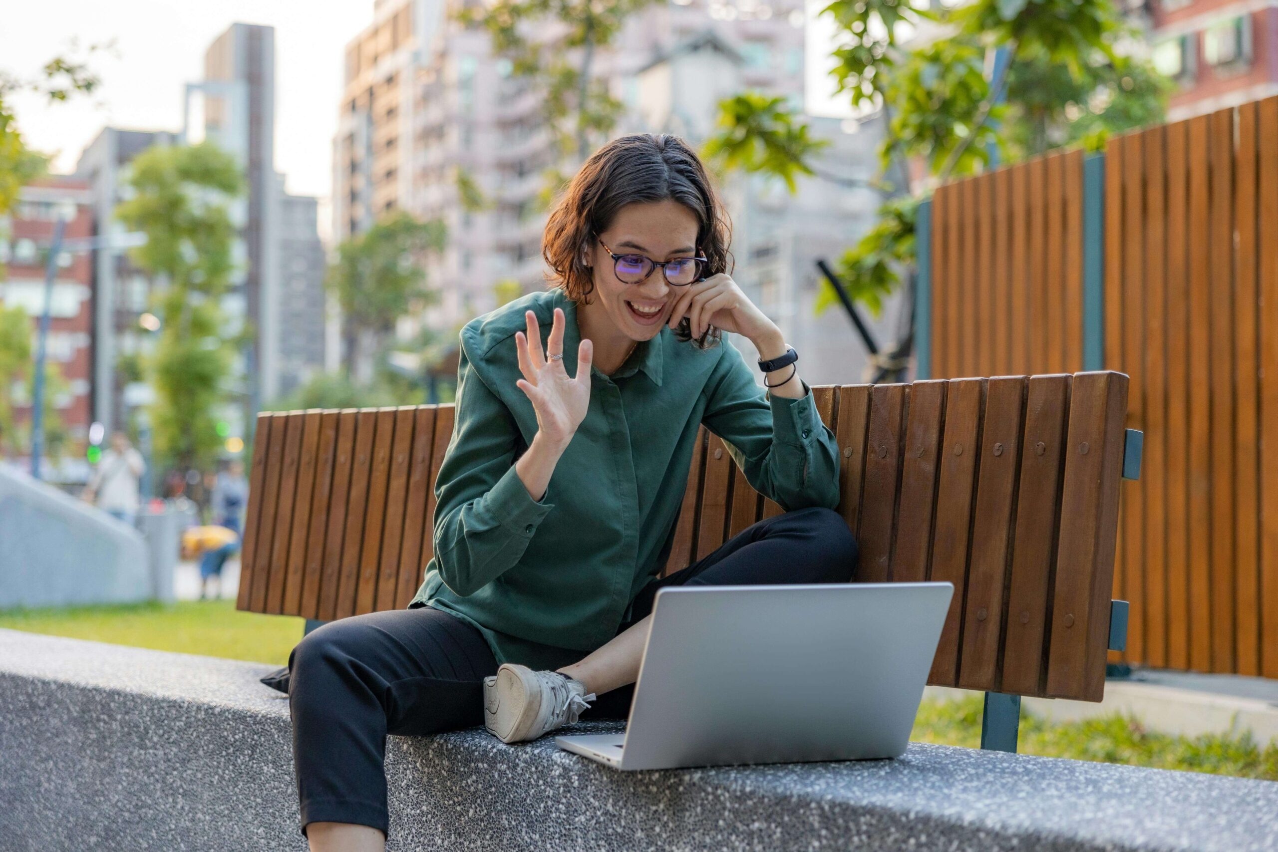 Smiling woman sitting outside on a bench waving at a laptop during a video call. Take accountability and move forward with eating disorder recovery coaching in England with a supportive eating disorder recovery coach.
