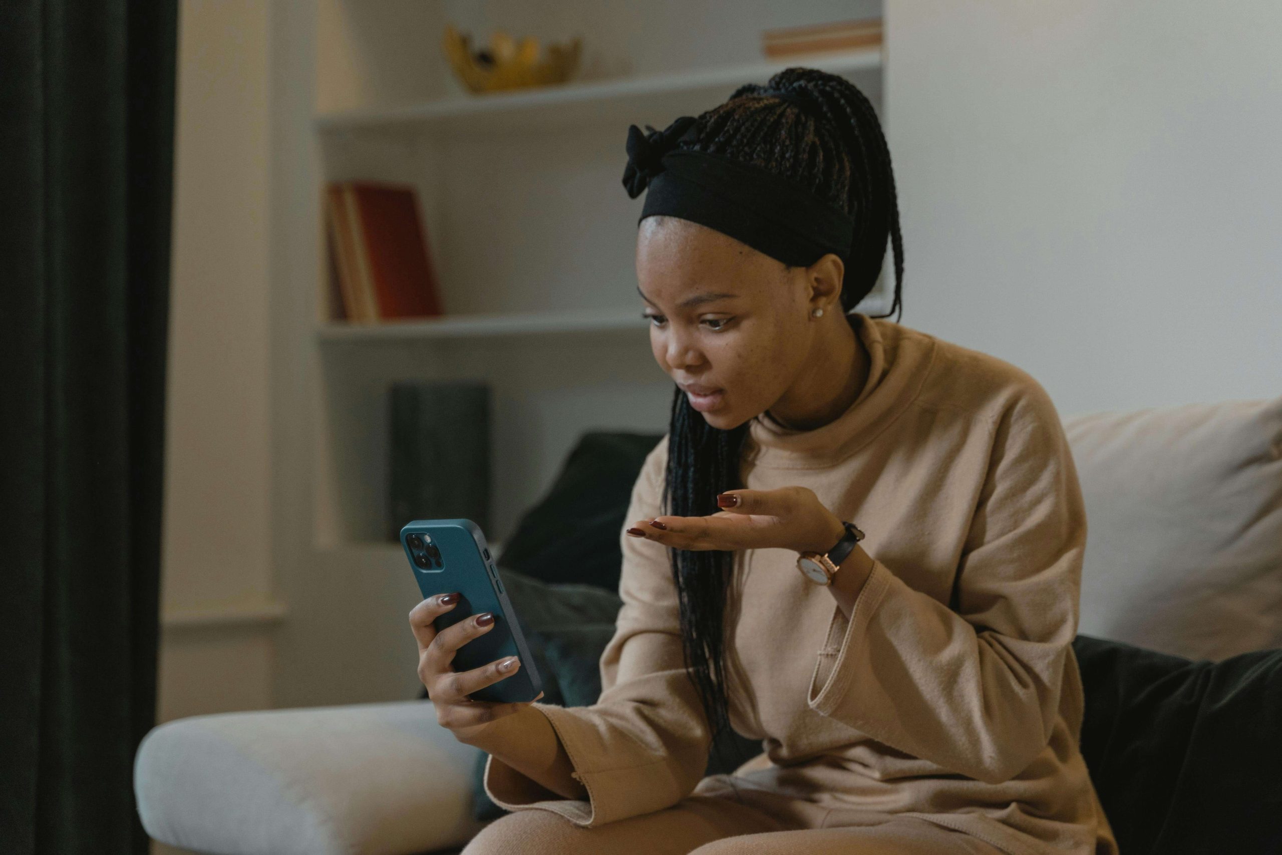 A woman sitting on a couch holding a phone during an online coaching session, appearing thoughtful and engaged in conversation. Find calm, connection, and guidance through eating disorder recovery online in England with compassionate coaching that supports you in everyday moments.