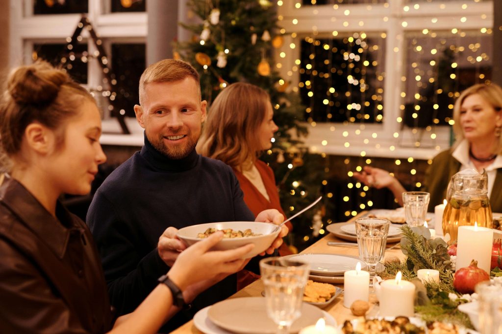 food | eating disorder recovery coach in england | anorexia recovery coaching | anorexia recovery | London | Brighton | Manchester A teenage girl passing a bowl of food to an adult at a warmly lit Christmas dinner surrounded by family and holiday decorations. Build supportive meal strategies this Christmas with anorexia recovery coaching in England to help you stay grounded during shared holiday meals.