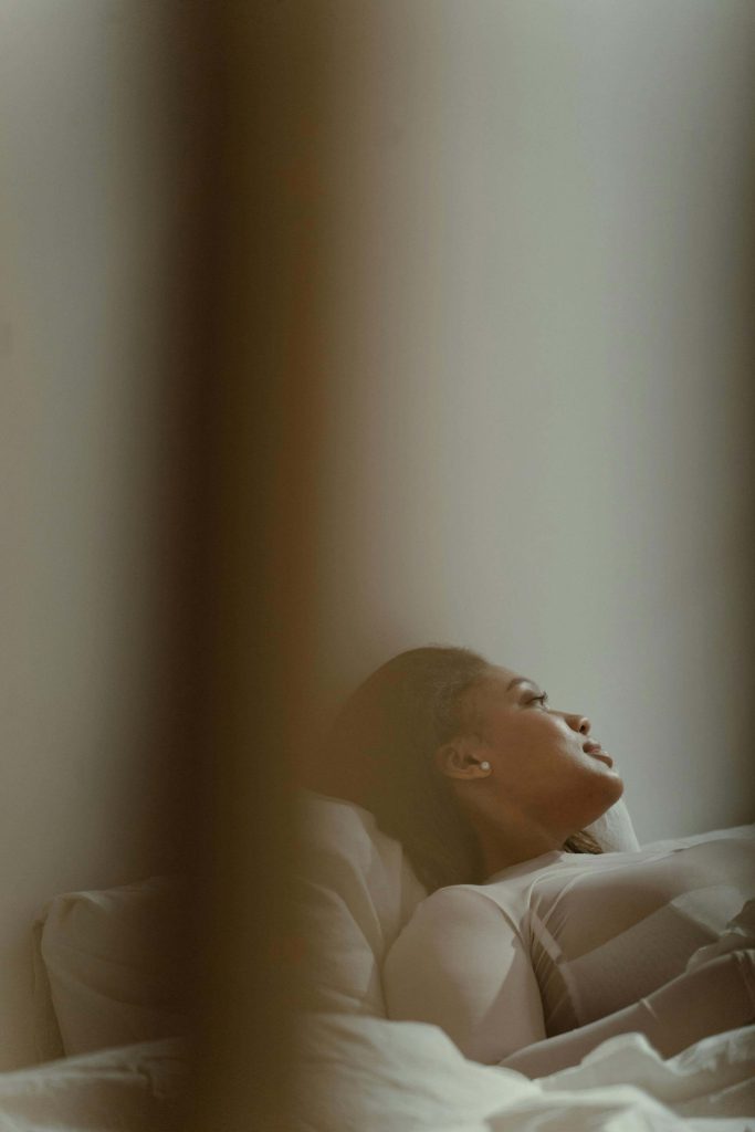 A woman rests in bed, gazing thoughtfully toward the light with a calm yet introspective expression. Through anorexia recovery coaching in England, you can find steady support as you make sense of shifting emotions and reconnect with the parts of yourself you thought were lost.