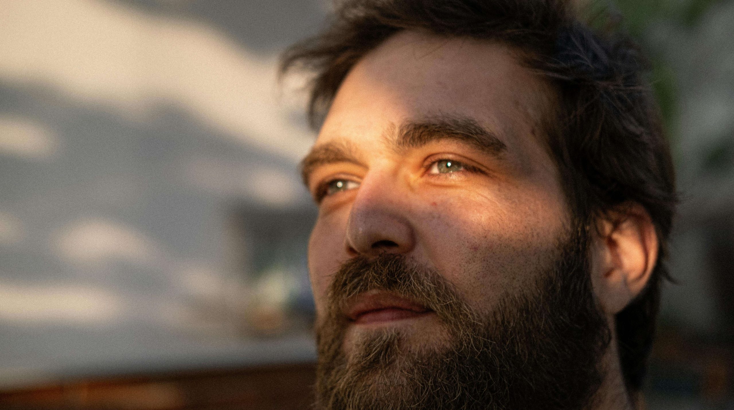 Man with beard looking upward thoughtfully in natural lighting. Build consistency in recovery with compassionate eating disorder recovery coaching in England.