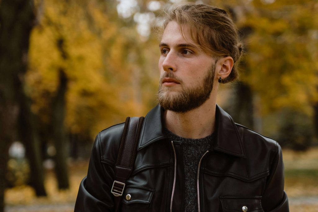 Man in leather jacket looking thoughtfully into the distance outdoors. Break free from hidden struggles with eating disorder recovery coaching in England that understands high-achieving lifestyles.