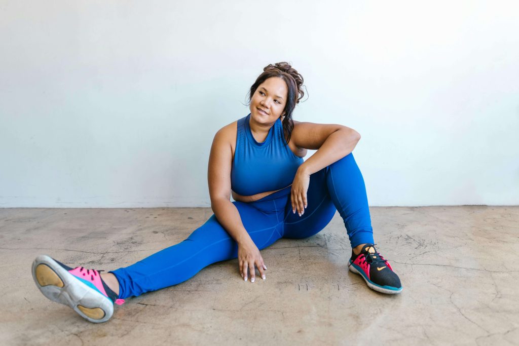 Woman in blue athletic wear sitting relaxed on a studio floor. Start healing from high-functioning eating disorders with specialized eating disorder recovery coaching in England.